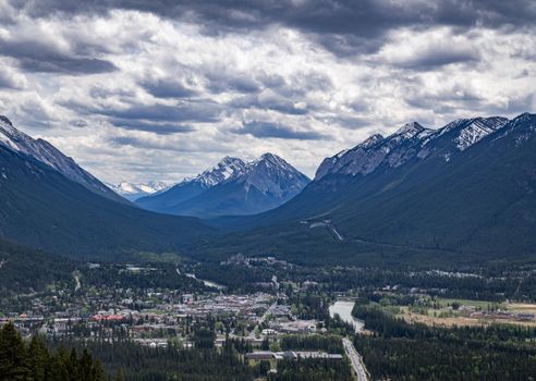 A breathtaking view of Banff town surrounded by mountain ranges under a dramatic cloudy sky.