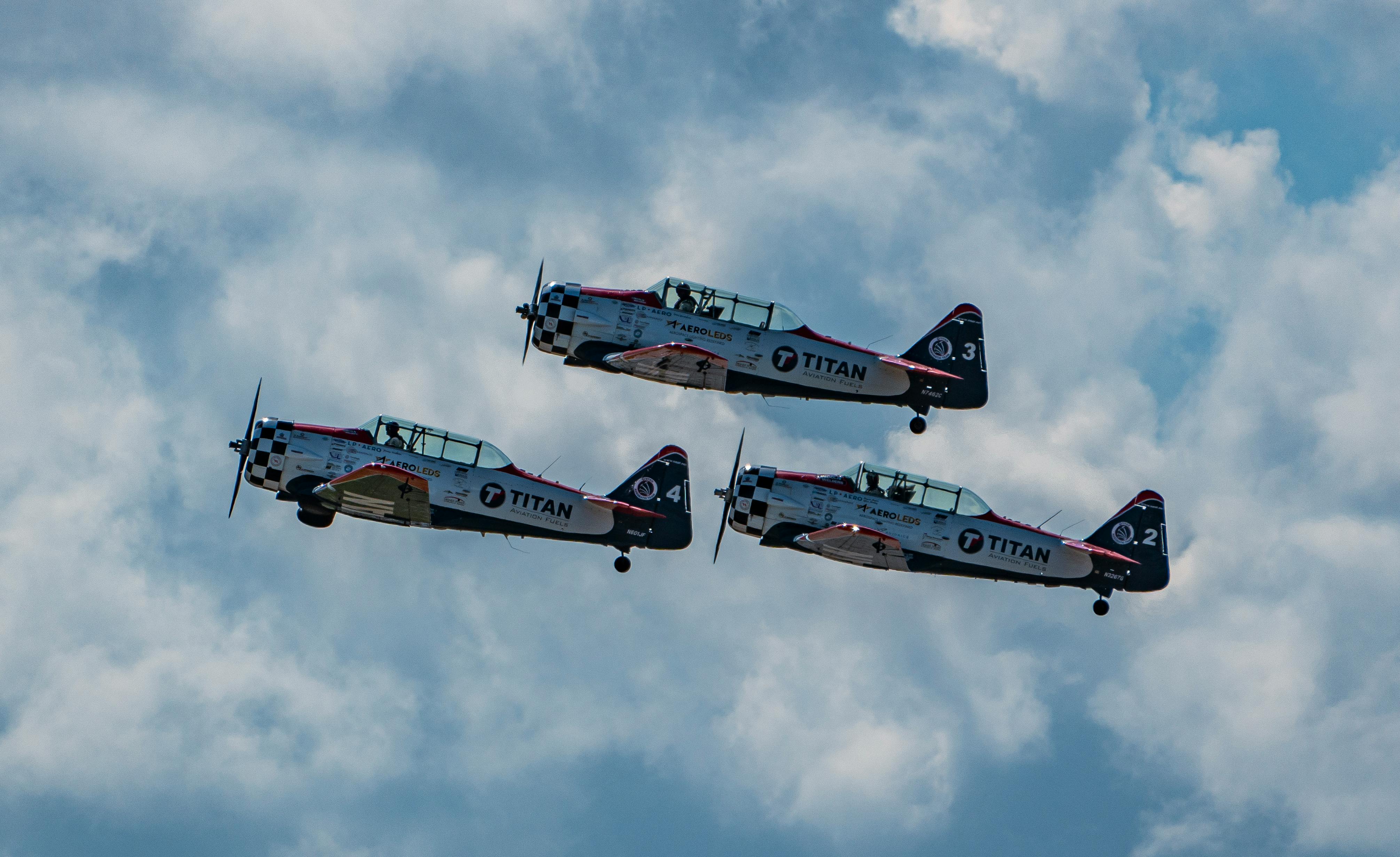 Three vintage aircrafts in formation against a backdrop of clouds during a daytime aerial display.