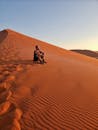 日落时分，一名男子坐在纳米布沙漠的沙丘上，享受着孤独