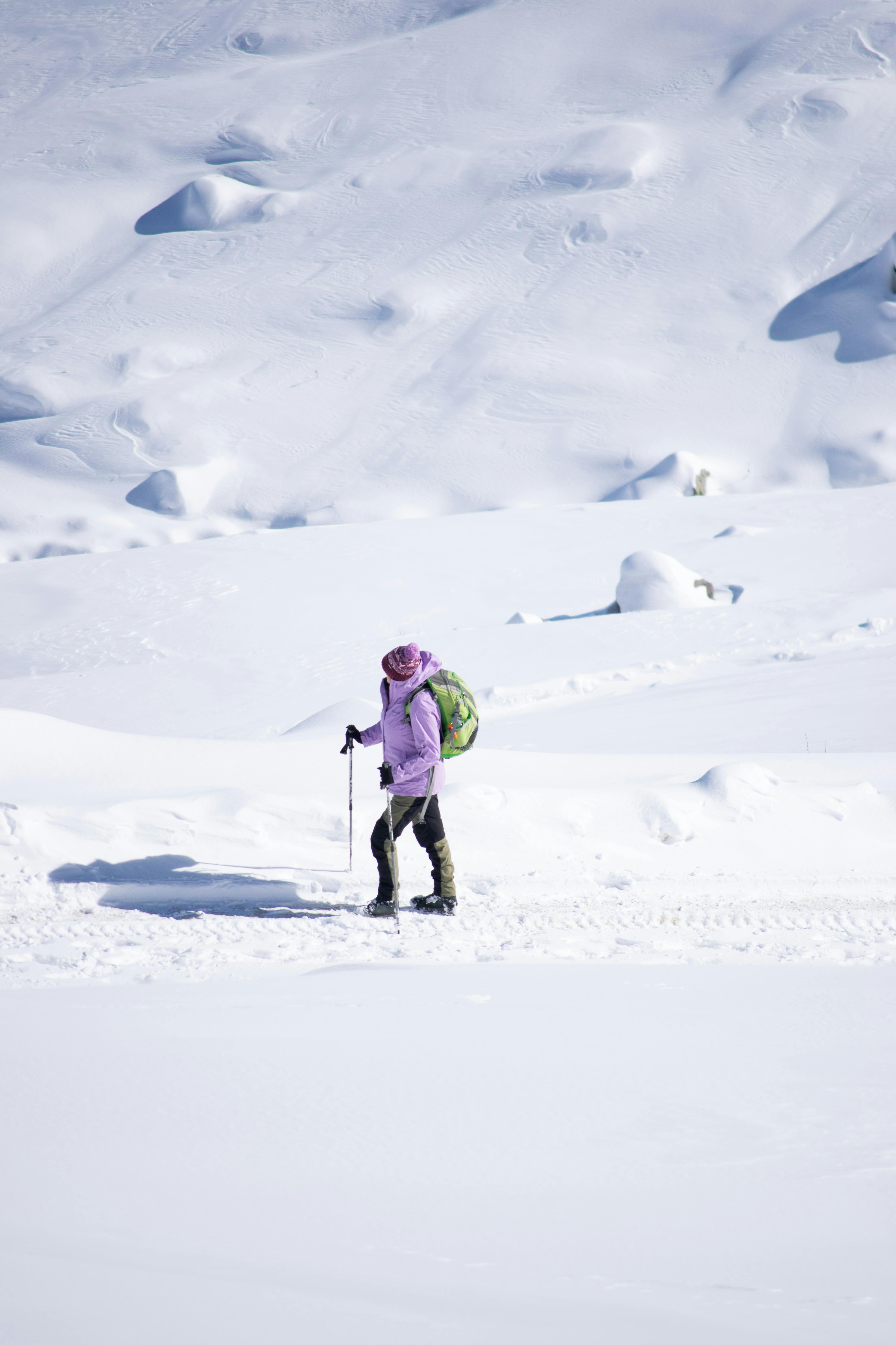A lone hiker traverses a vast snowy landscape with snowshoes and a backpack during winter.