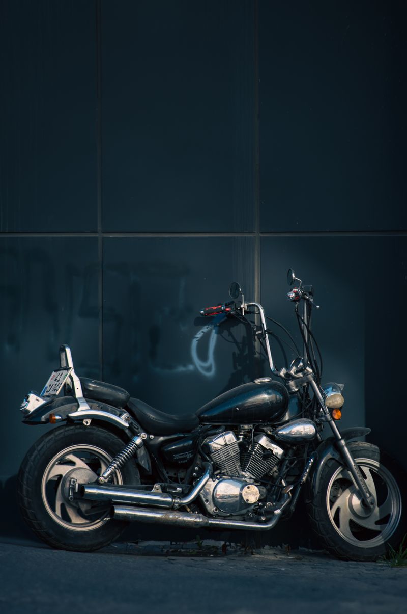 A classic cruiser motorcycle with chrome accents parked against a dark urban wall