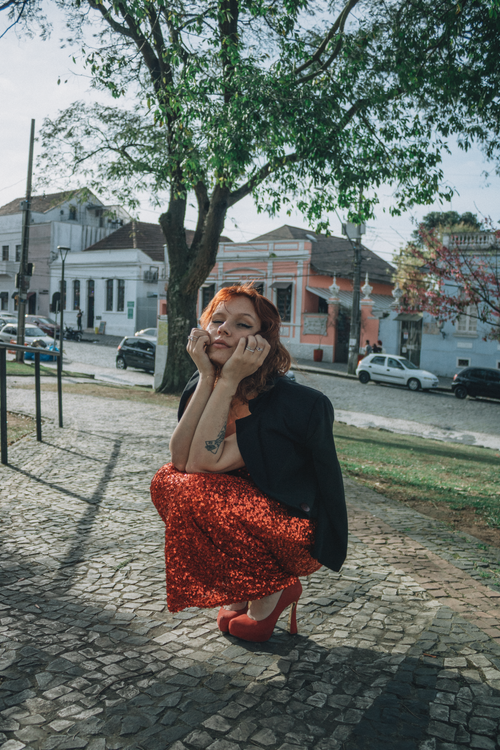 Free Fashionable woman in red dress posing under trees on cobblestone path. Stock Photo