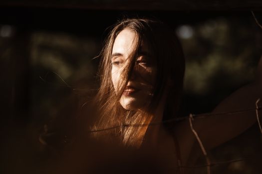 Artistic portrait of a woman in sunlight with hair blowing across her face.