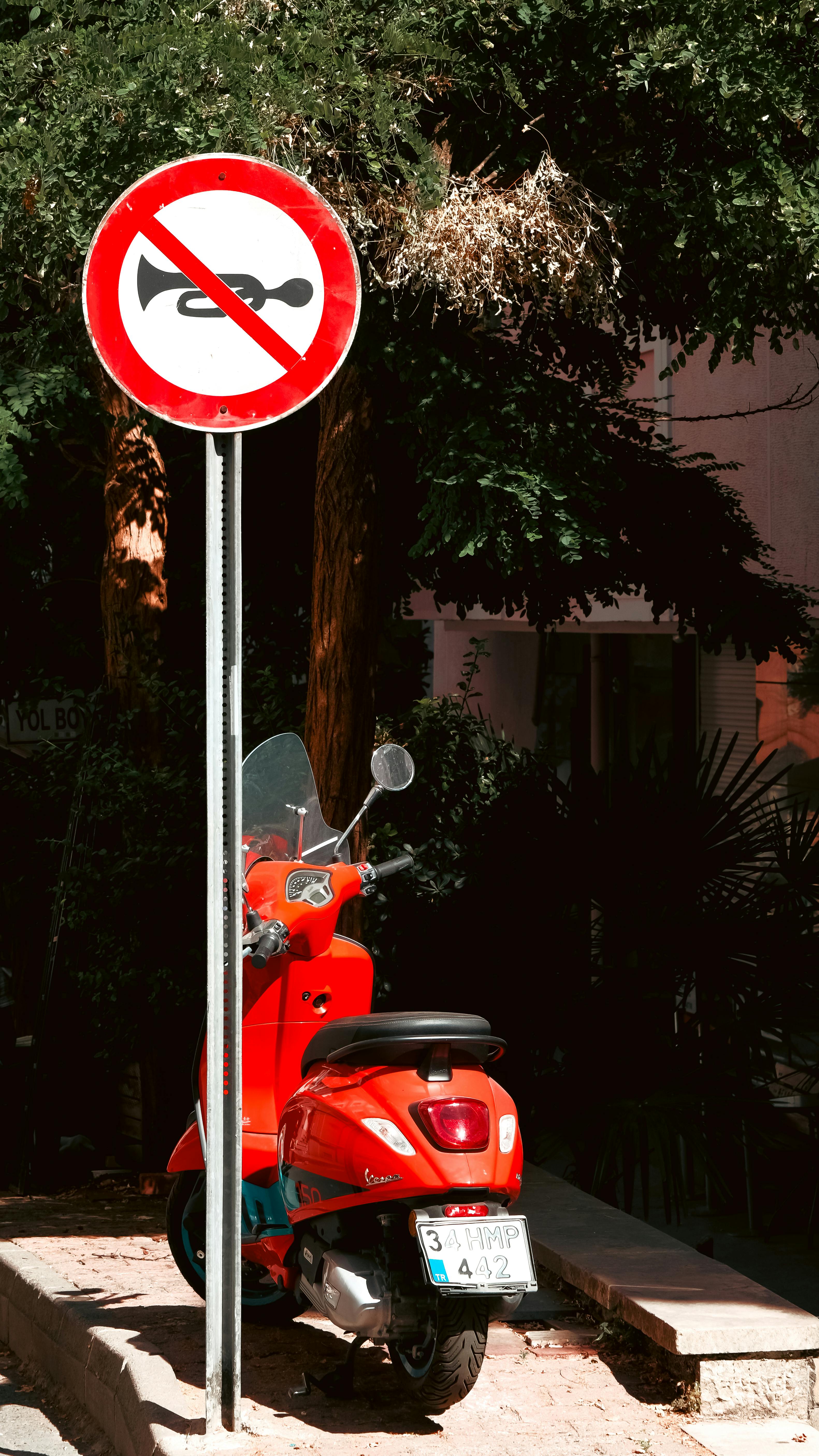 Vibrant red scooter parked under a no horn sign, capturing urban vibes.
