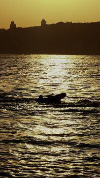 A lone boat silhouetted on a shimmering sea during a golden sunset.