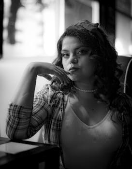 Dramatic black and white portrait of a woman sitting in a cafe, showcasing elegance and contemplative mood.