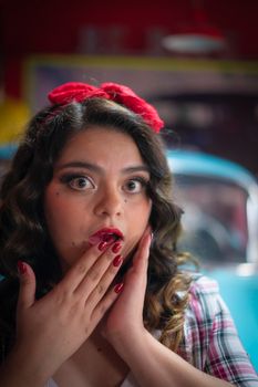 A surprised woman in retro style with red lipstick and headband against a vintage car background.