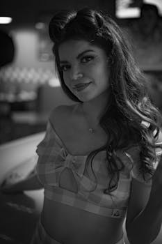 Black and white portrait of a woman in retro 1950s fashion with a soft smile and vintage hairstyle.