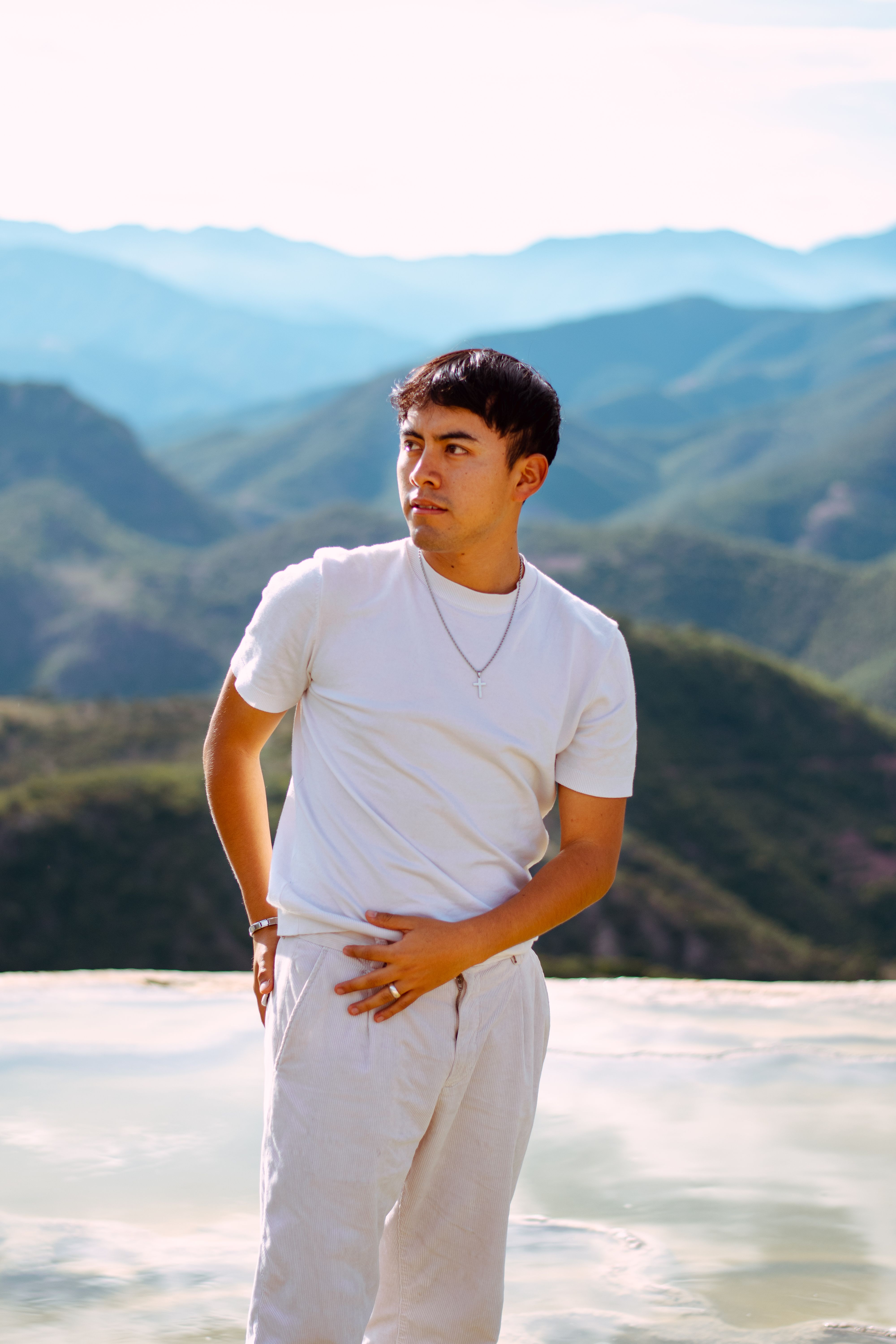 Young man in white outfit posing against Oaxaca's stunning mountain backdrop.