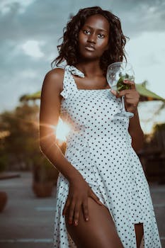 一位时尚女士身着圆点连衣裙，端着酒杯，在温暖的阳光下拍照
