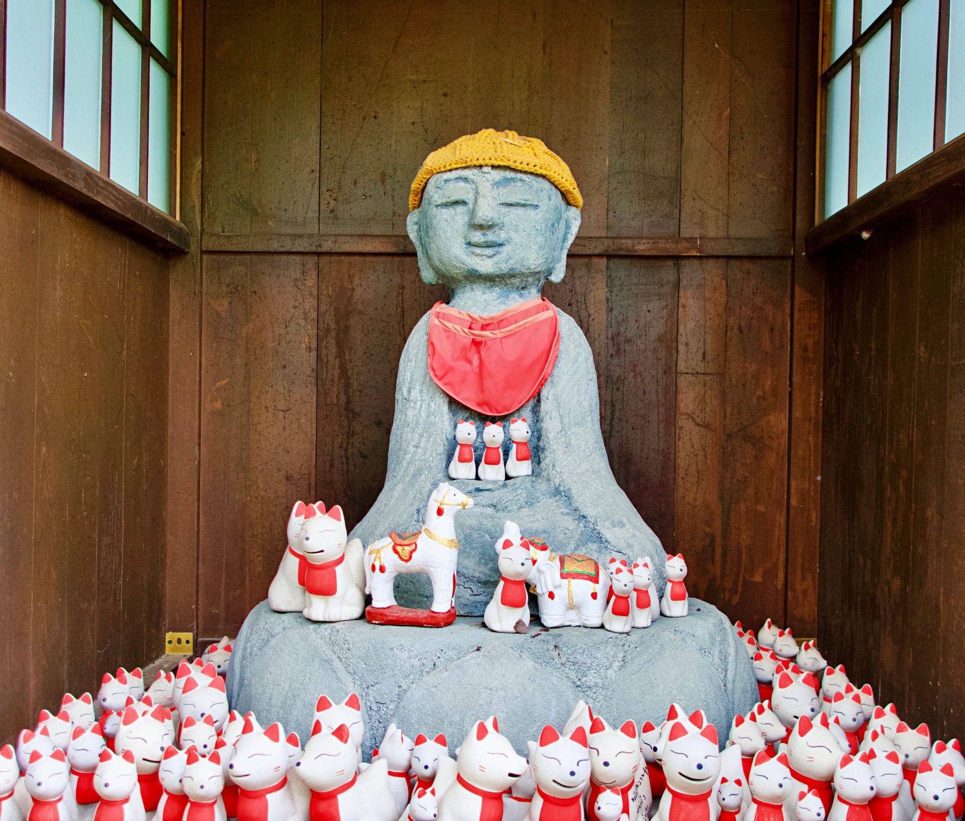 A serene stone Buddha surrounded by Maneki-neko figurines in a traditional Japanese shrine.
