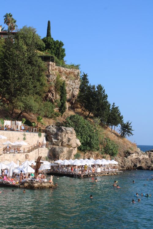Free Crowded beach by rocky cliffs with umbrellas and swimmers, perfect for a summer getaway. Stock Photo