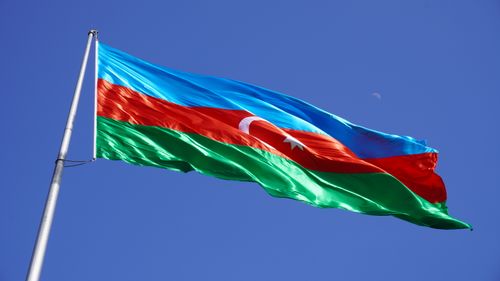 Free Vibrant Azerbaijan flag waving against a bright blue sky, symbolizing national pride and freedom. Stock Photo