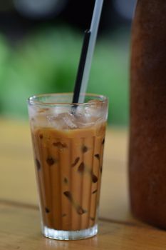 Close-up of a refreshing iced coffee with a black straw and ice cubes on a wooden table.