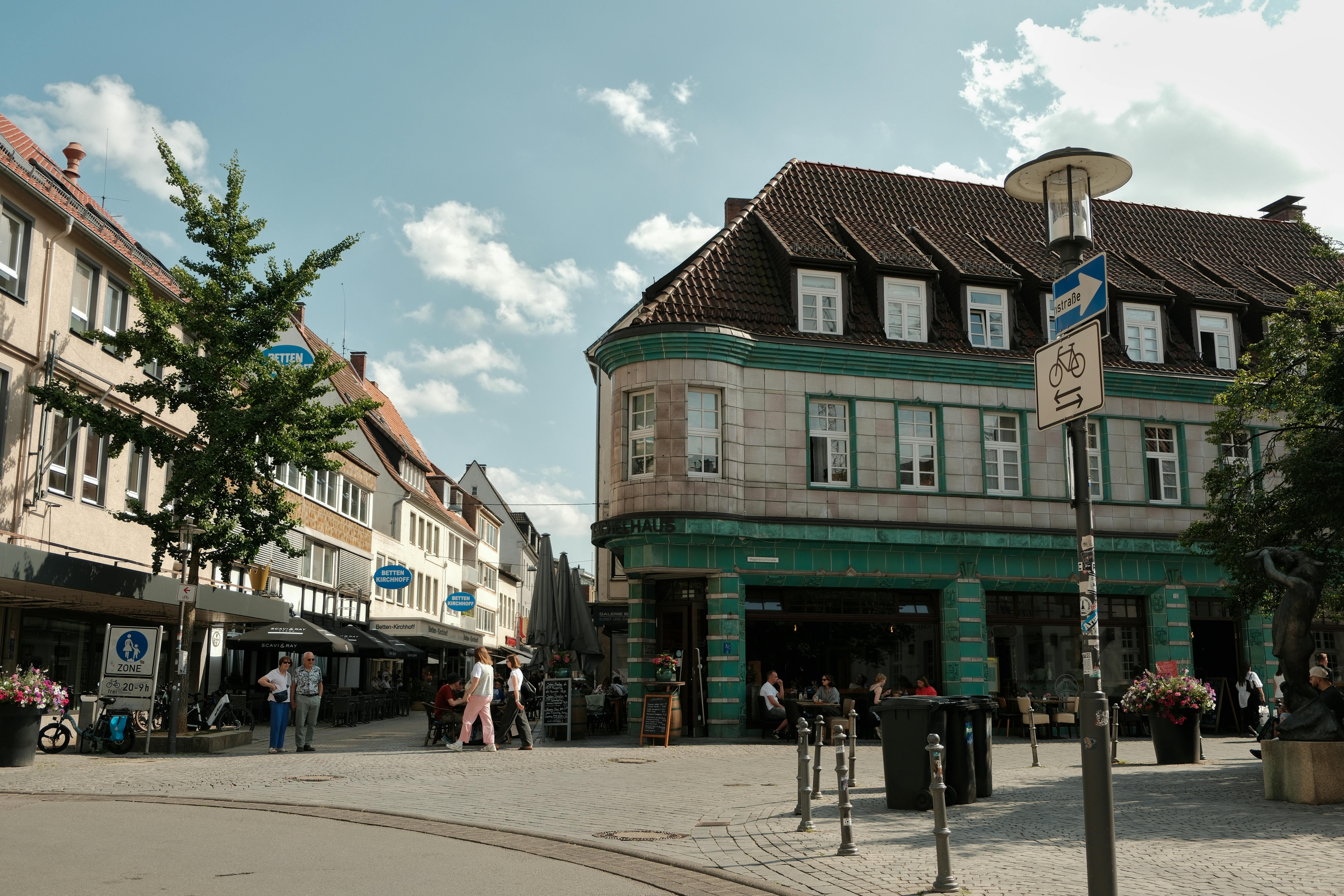Sunny day at a quaint plaza in Bielefeld, Germany with classic architecture and pedestrians.