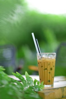 Chilled iced coffee with straws on an outdoor table surrounded by lush greenery.