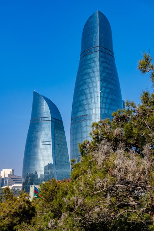Free Flame Towers in Baku, Azerbaijan rise above the trees against a clear blue sky. Stock Photo