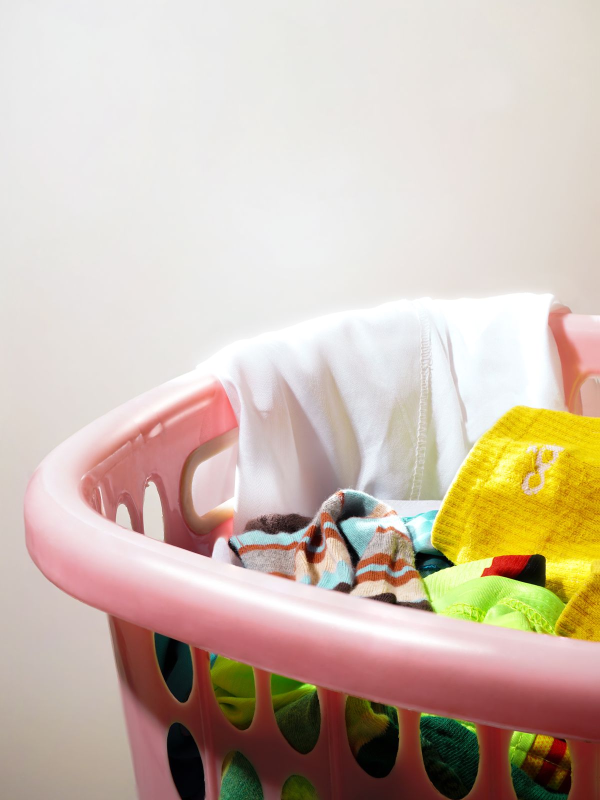 Pink laundry basket filled with colorful clothes, used as a color-coded kids' basket
