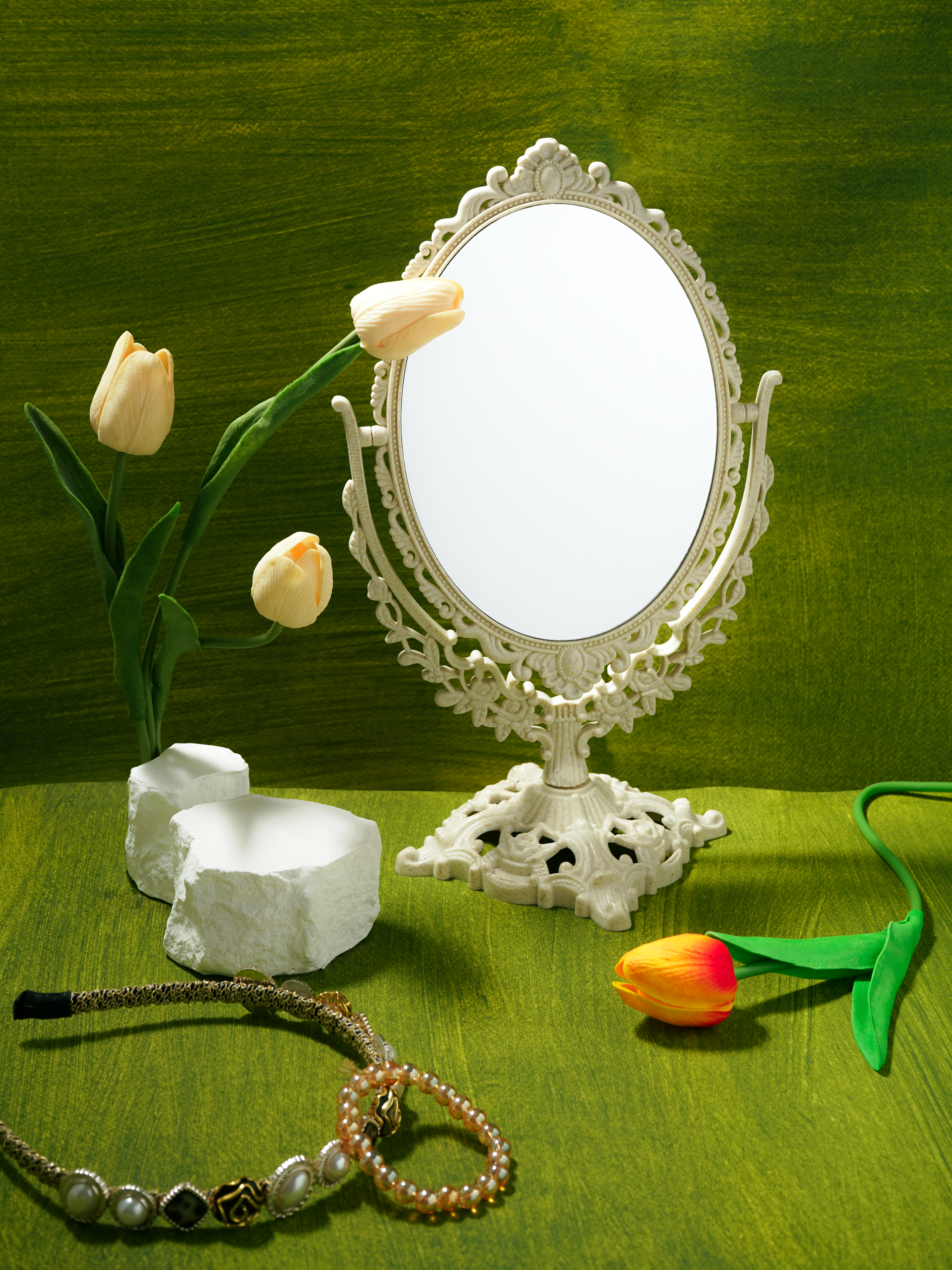 Ornate vintage mirror with tulips and jewelry on a textured green backdrop.