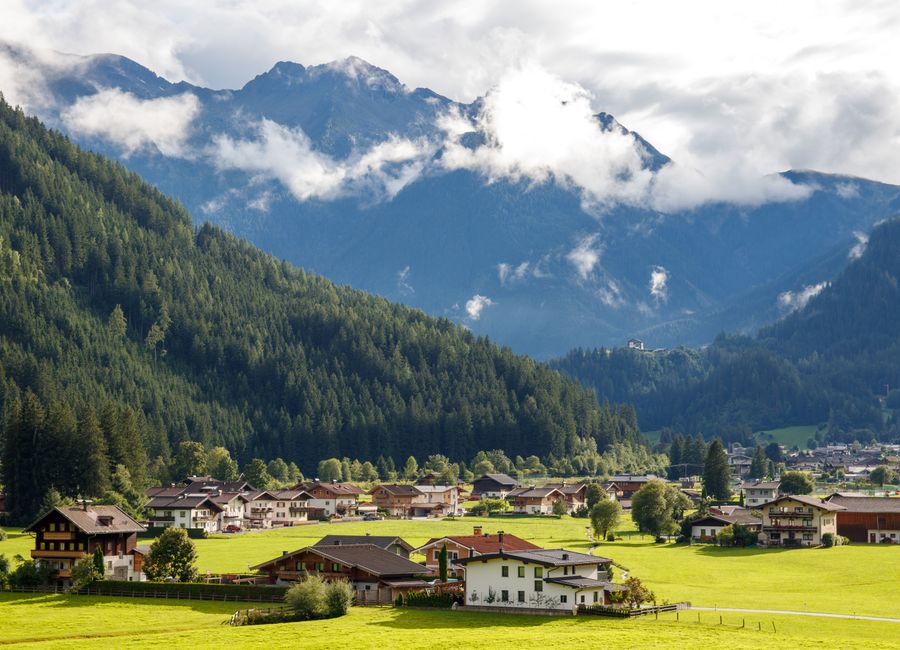 Charming Alpine village nestled against dramatic mountain backdrop under a cloudy sky.