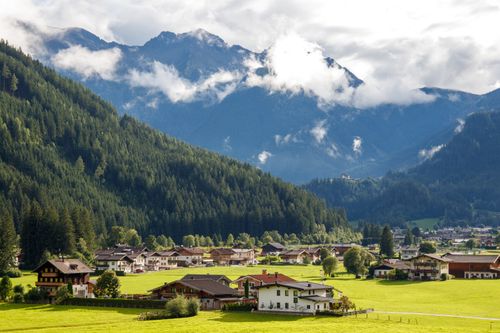Free Charming Alpine village nestled against dramatic mountain backdrop under a cloudy sky. Stock Photo