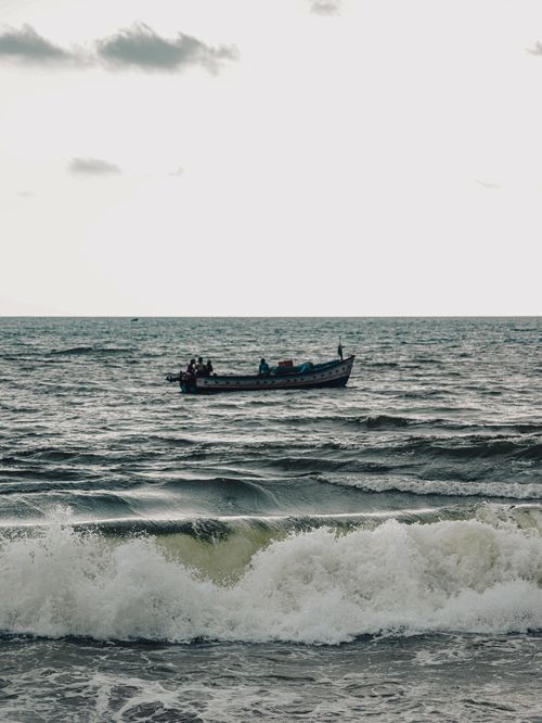 Free A fishing boat sails on the ocean as waves crash in the foreground under a cloudy sky. Stock Photo