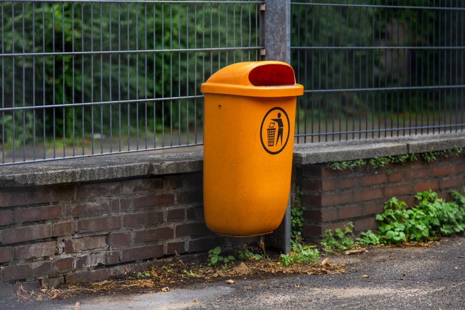 A vibrant orange trash bin mounted on a brick wall in an urban street setting.