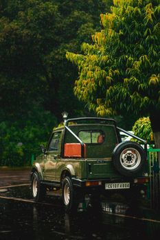 A green off-road vehicle parked under a tree on a rainy street.