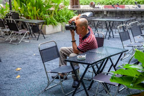 Free Man photographing at an outdoor cafe surrounded by empty chairs. Stock Photo