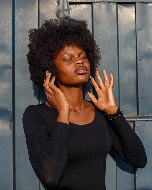 Free A woman with afro hairstyle stands calmly, eyes closed, outdoors in sunlight. Stock Photo