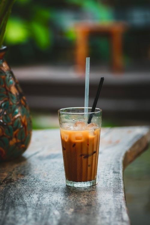 Free Glass of iced coffee with straws on rustic wooden table, outdoor garden setting. Stock Photo