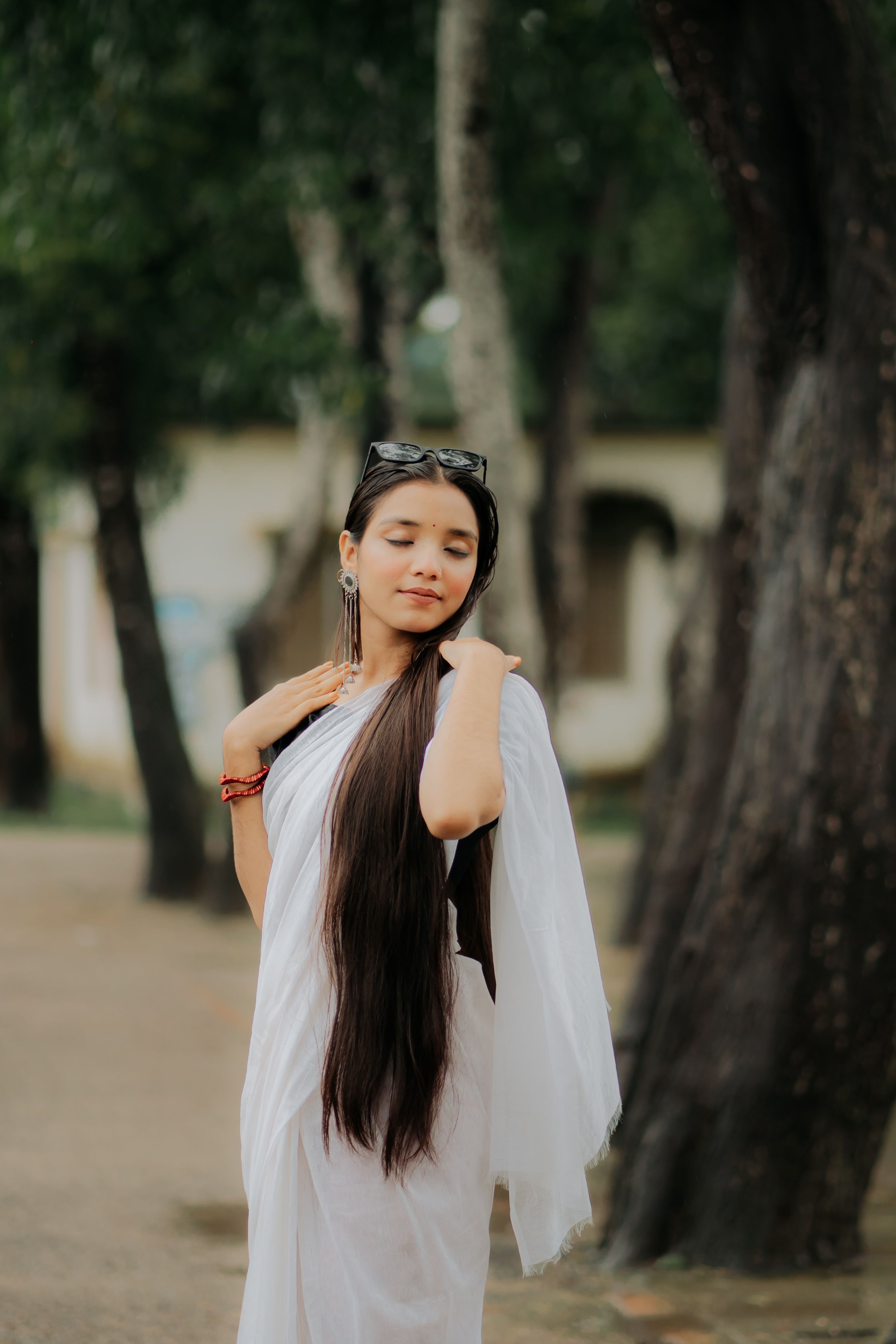Peaceful woman with long hair in white dress surrounded by trees outdoors.
