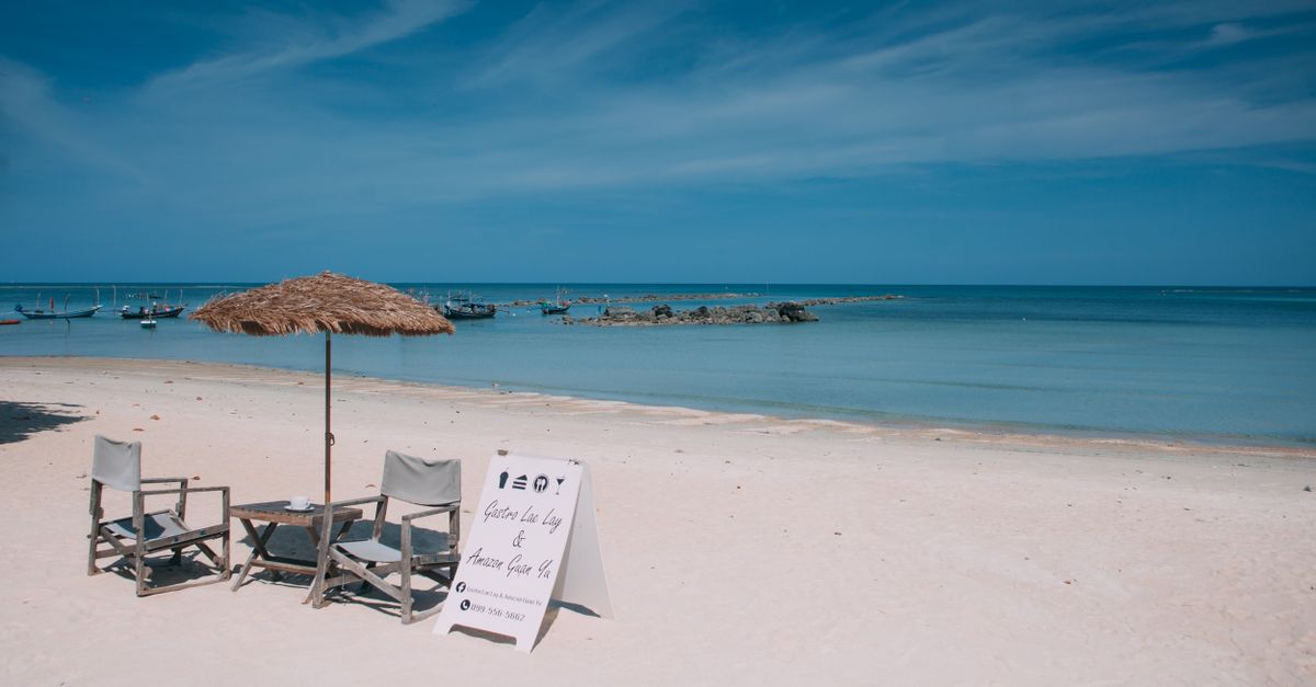 Relaxing beach view on Koh Samui with chairs and parasol under the sunny sky.