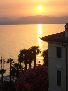 Beautiful sunset view over Lake Garda with palm trees and vibrant colors in Lazise, Italy.