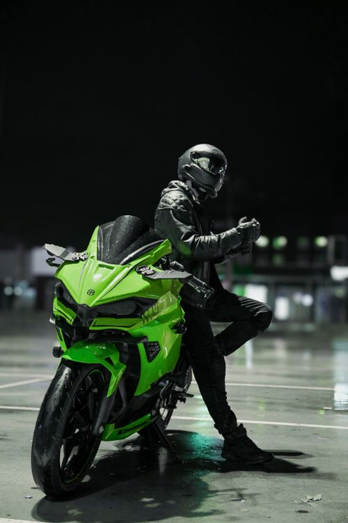 Free Stylish motorcyclist in helmet and leather suit poses with green motorcycle in nighttime urban setting. Stock Photo