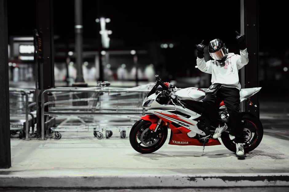 A motorcyclist in gear poses confidently on a Yamaha sportbike in an urban setting at night.