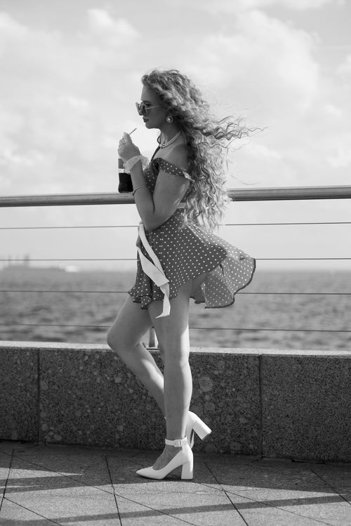 Free Fashionable woman in polka dot dress drinks and enjoys seaside breeze. Stock Photo