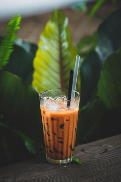 Free Glass of iced Thai tea set against lush green leaves for a tropical feel. Stock Photo