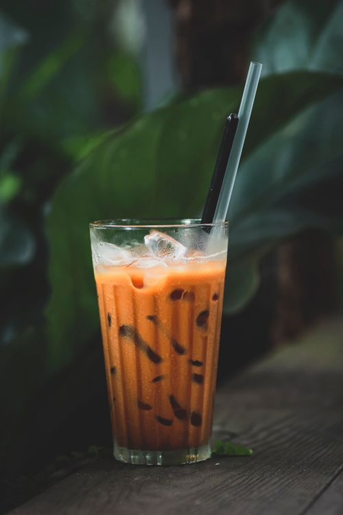 Free Chilled glass of iced Thai tea on a wooden table surrounded by green plants. Stock Photo