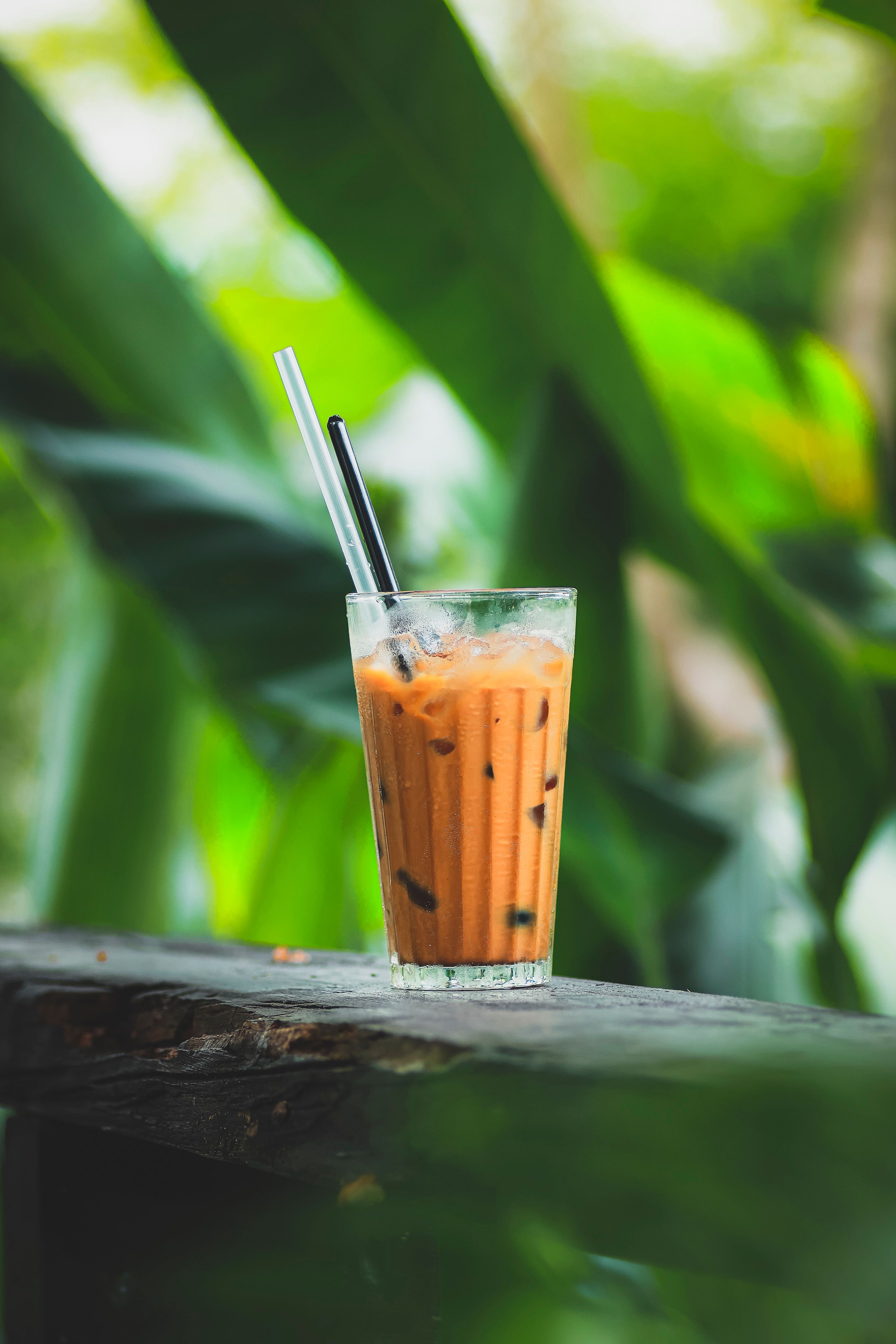 A tall glass of orange Thai iced tea layered with creamy evaporated milk on top, served over ice with a straw.