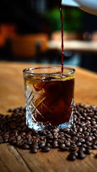 Cold brew coffee poured into a glass surrounded by coffee beans on a wooden table in Niğde, Türkiye.