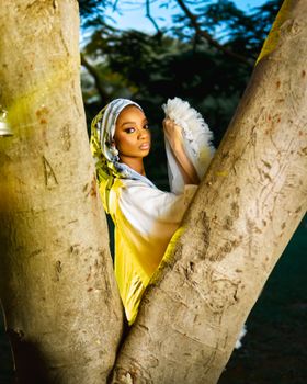 Woman in a chic outfit stands between tree branches, embracing nature at daytime.