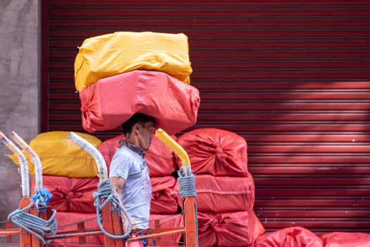 A man carrying stacked red and yellow packages outdoors in an urban setting.