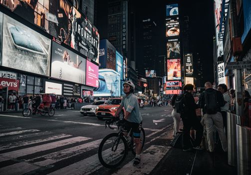 Bustling Times Square night scene featuring illuminated billboards and a cyclist on a city street.
