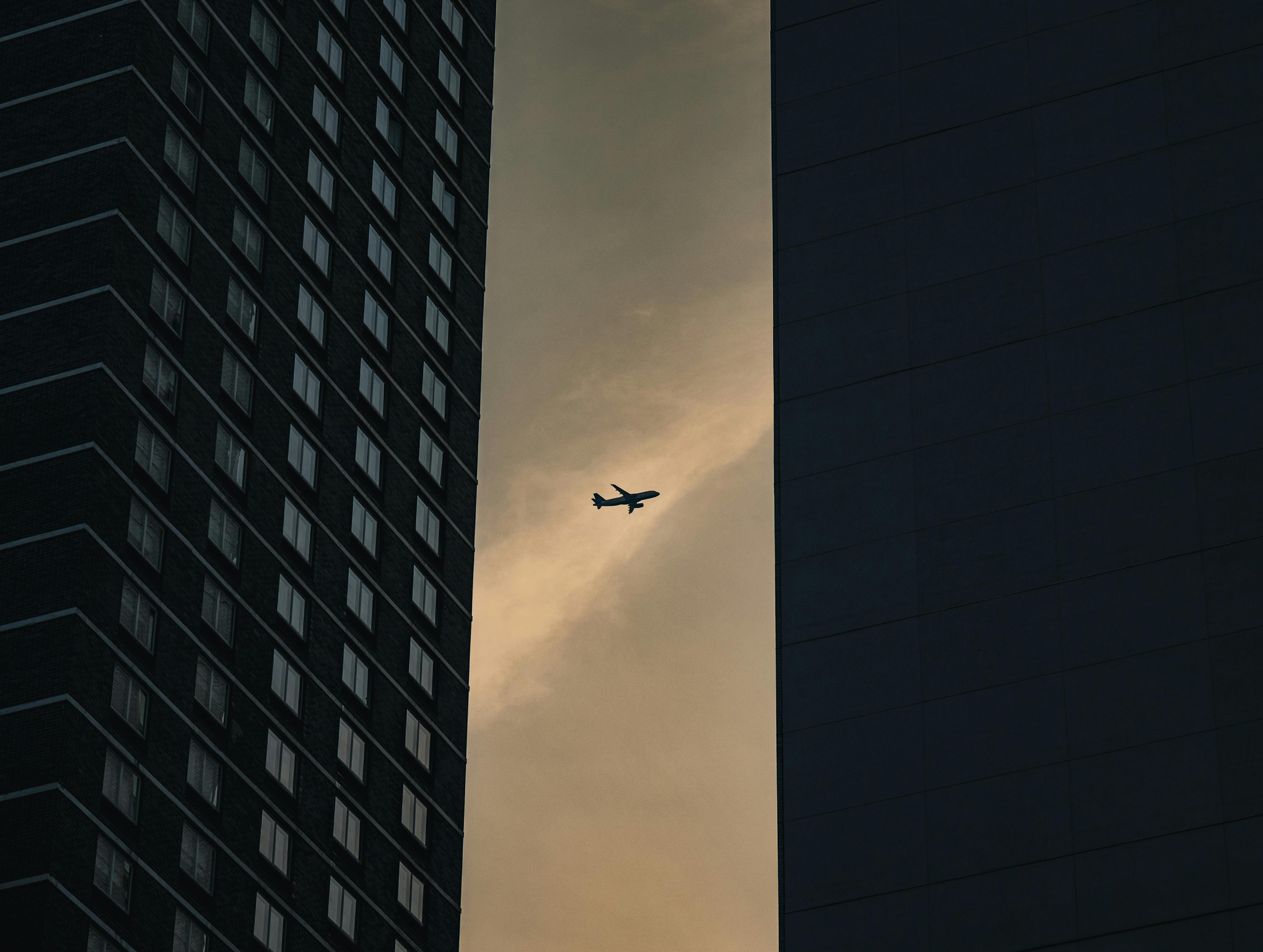 A dramatic view of an airplane between skyscrapers against a dusky sky in New York City.
