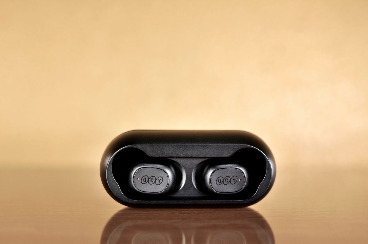 Black wireless Bluetooth earbuds in a case against a warm reflective background