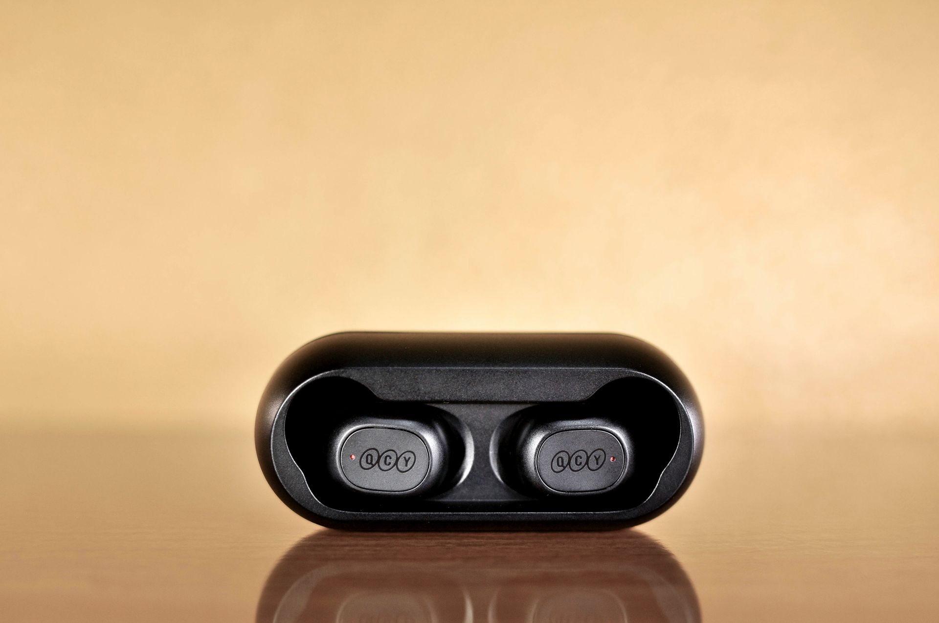 Black wireless Bluetooth earbuds in a case against a warm, reflective background.