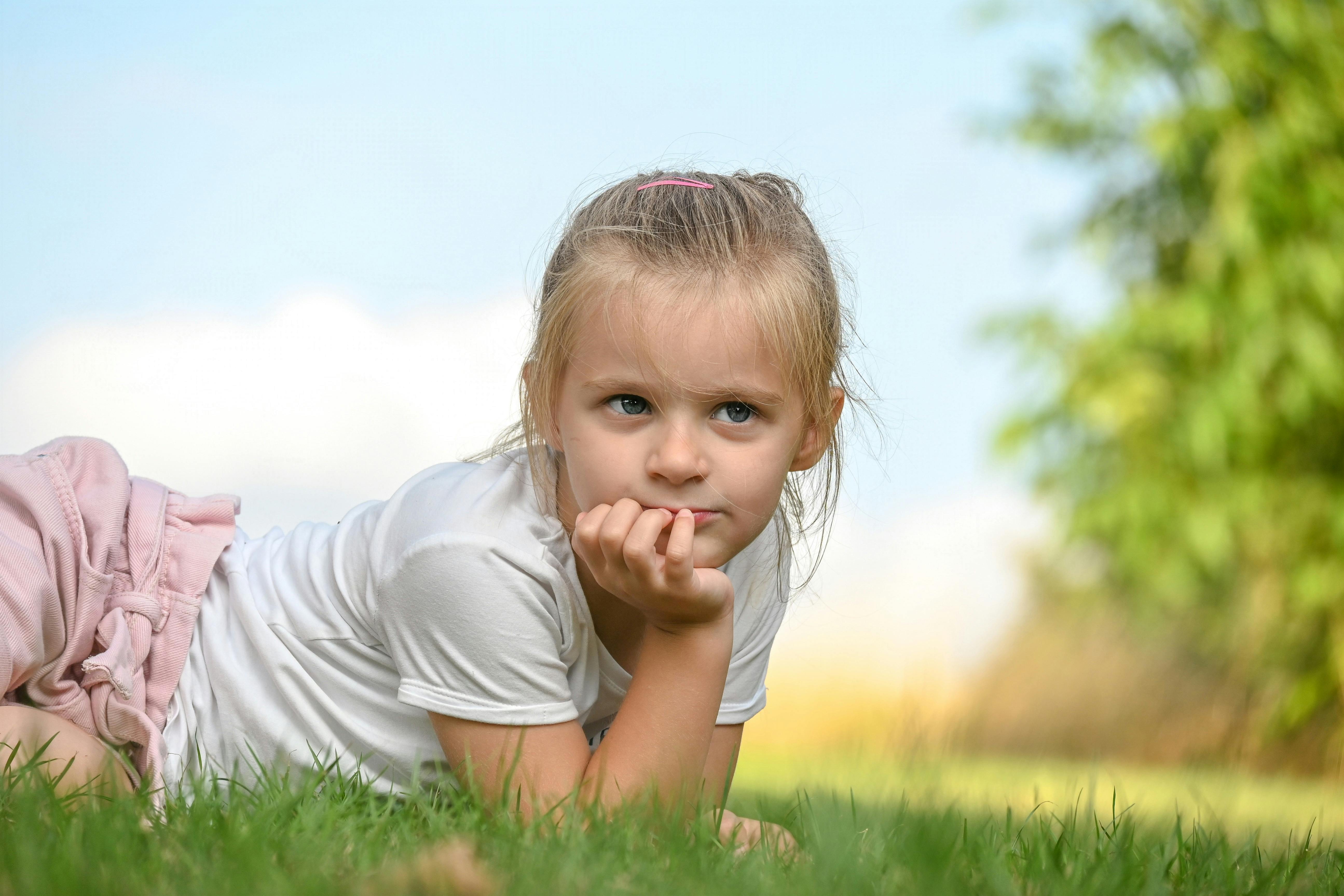 A young girl lies on the grass, daydreaming on a sunny day, with a peaceful and thoughtful expression.