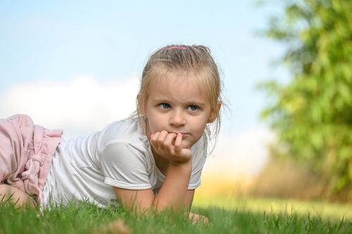 Free A young girl lies on the grass, daydreaming on a sunny day, with a peaceful and thoughtful expression. Stock Photo