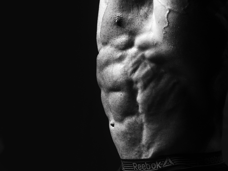 Dramatic black and white photo of a muscular male torso highlighting defined abs.
